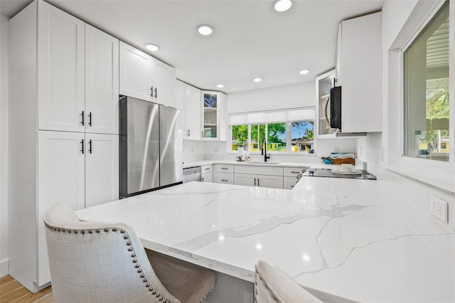 kitchen with stainless steel appliances, light stone countertops, glass insert cabinets, and recessed lighting