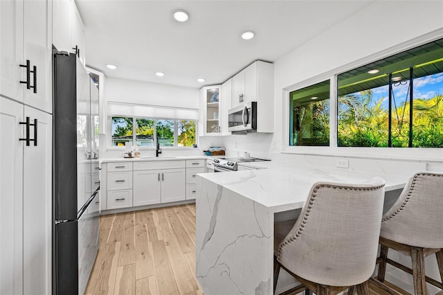 kitchen with a peninsula, appliances with stainless steel finishes, white cabinets, and light wood-style floors