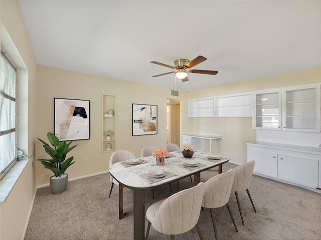 dining space featuring baseboards, built in features, visible vents, ceiling fan, and light colored carpet