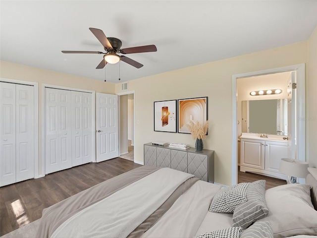 bedroom featuring ensuite bath, a ceiling fan, visible vents, multiple closets, and dark wood-style floors