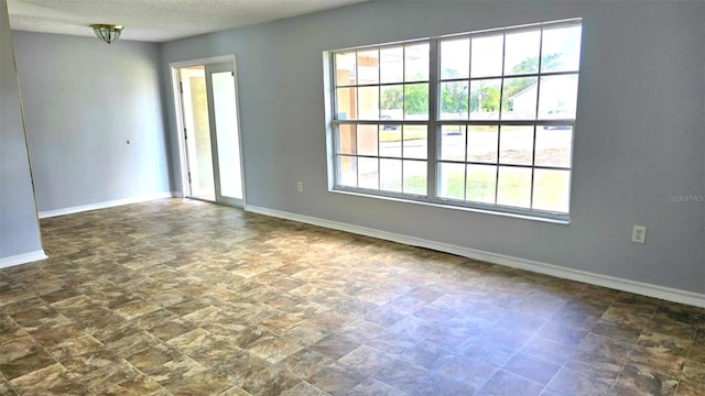 empty room featuring stone finish flooring, baseboards, and a textured ceiling