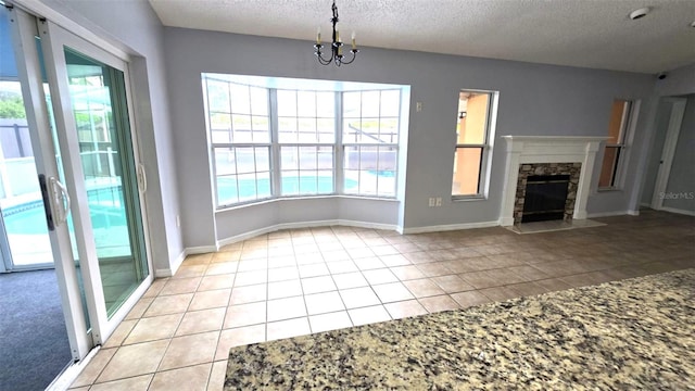 unfurnished living room featuring light tile patterned floors, a fireplace, a textured ceiling, a notable chandelier, and baseboards