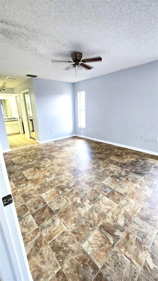 empty room with stone finish floor, baseboards, a ceiling fan, and visible vents