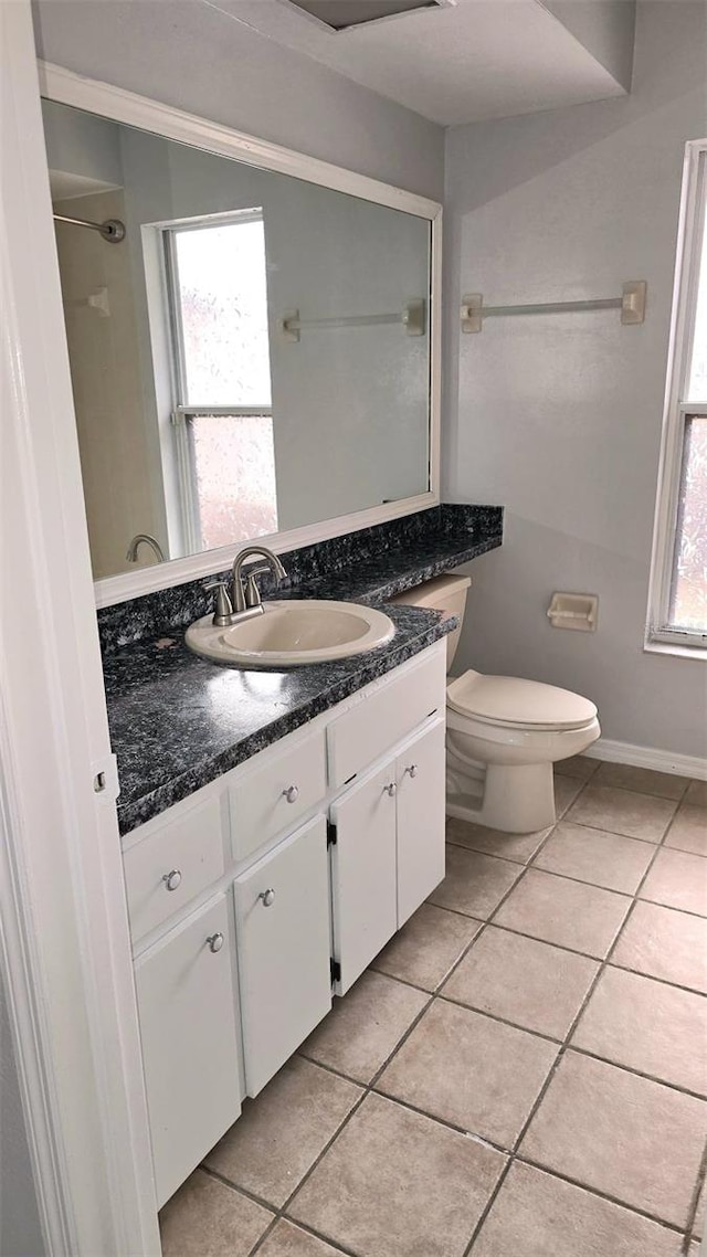bathroom with toilet, vanity, tile patterned flooring, and a wealth of natural light
