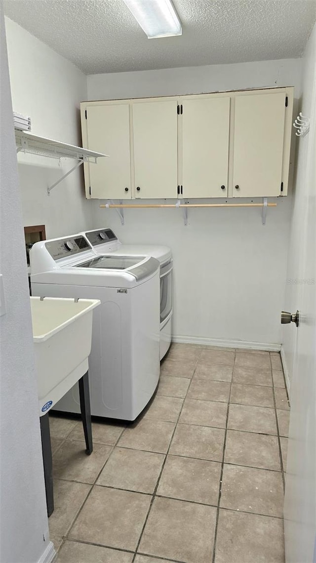 washroom with cabinet space, light tile patterned floors, washing machine and dryer, and a textured ceiling