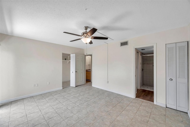 1655 S Highland Ave Unit D140, Clearwater, FL 33756 - unfurnished bedroom featuring a textured ceiling, baseboards, connected bathroom, light tile patterned floors, and a spacious closet