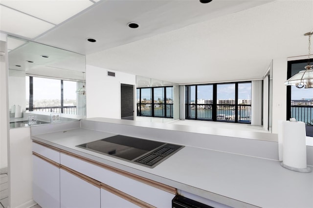 kitchen featuring white cabinets, visible vents, black electric stovetop, light countertops, and decorative light fixtures