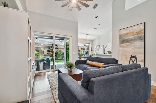 living area featuring high vaulted ceiling, visible vents, ceiling fan with notable chandelier, and wood finished floors
