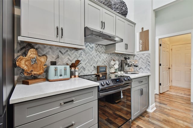 kitchen featuring tasteful backsplash, gray cabinets, stainless steel electric range oven, light countertops, and under cabinet range hood