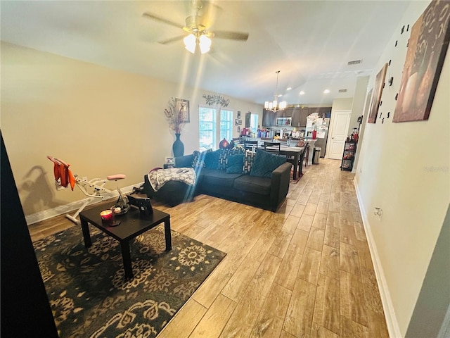 living room with light wood-type flooring, ceiling fan with notable chandelier, and baseboards