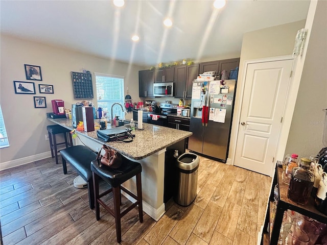 kitchen featuring light stone countertops, light wood-type flooring, recessed lighting, a breakfast bar, and appliances with stainless steel finishes