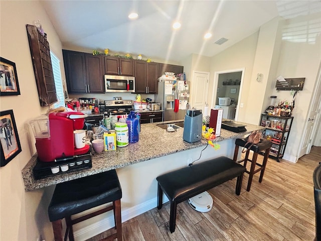 kitchen with light wood-style floors, visible vents, lofted ceiling, stainless steel appliances, and a breakfast bar area