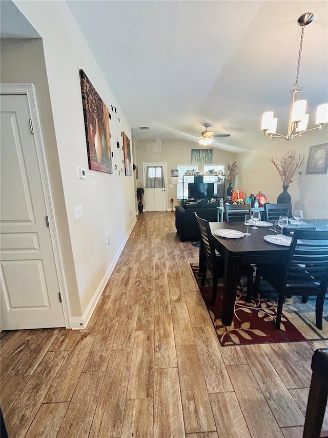 dining space featuring light wood finished floors, vaulted ceiling, and ceiling fan with notable chandelier