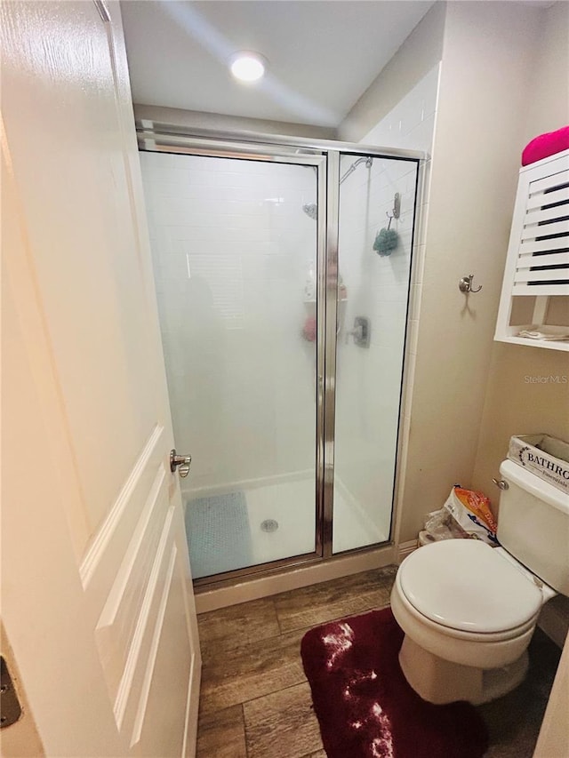 bathroom with toilet, a stall shower, and wood finished floors