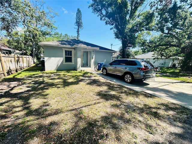 view of front facade with a front yard, driveway, stucco siding, and fence