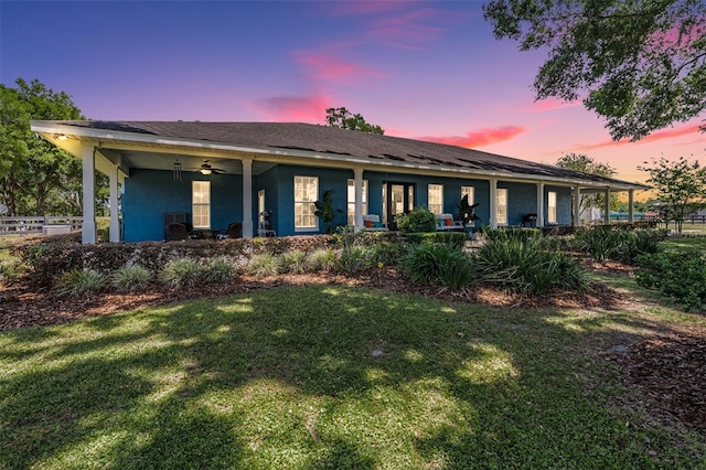 25601 Hutcheson Ln, Sorrento, FL 32776 - back of property at dusk featuring a lawn, ceiling fan, stucco siding, and fence