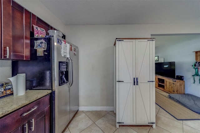 kitchen featuring stainless steel fridge with ice dispenser, light tile patterned floors, dark brown cabinets, light stone counters, and baseboards