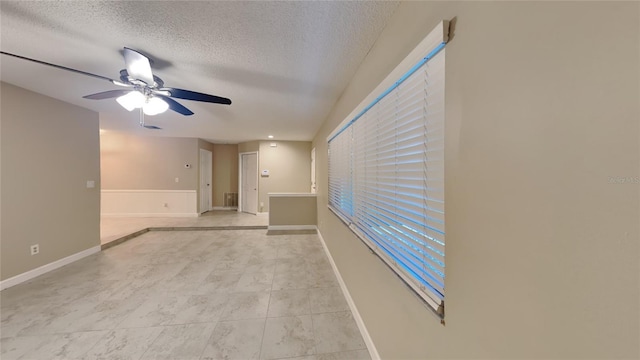 empty room with a textured ceiling, ceiling fan, and baseboards