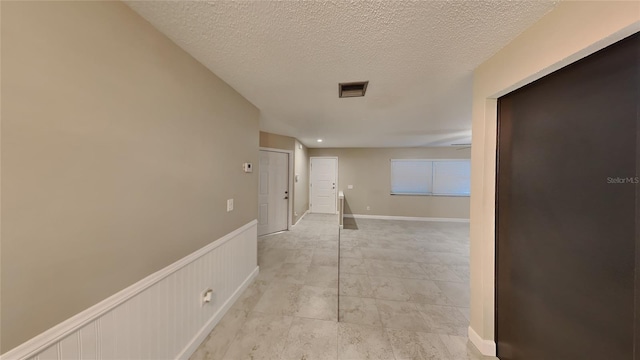 corridor with visible vents, a wainscoted wall, and a textured ceiling
