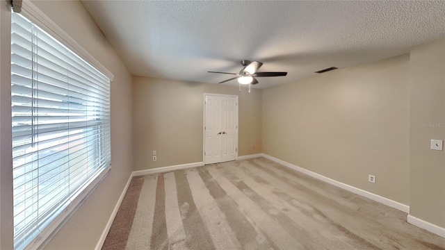 empty room featuring visible vents, light colored carpet, a textured ceiling, and ceiling fan
