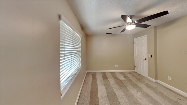 unfurnished room with ceiling fan, light colored carpet, baseboards, and a textured ceiling