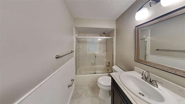 bathroom featuring combined bath / shower with glass door, toilet, a textured ceiling, vanity, and wainscoting