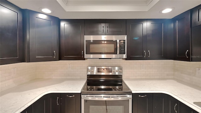 kitchen featuring stainless steel appliances, a tray ceiling, backsplash, and light stone counters