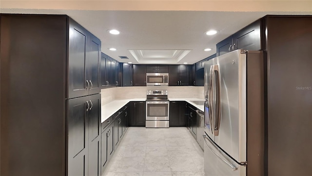 kitchen with a tray ceiling, tasteful backsplash, recessed lighting, light countertops, and stainless steel appliances