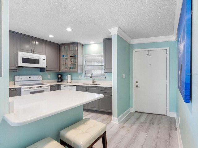 kitchen featuring white appliances, glass insert cabinets, gray cabinetry, light wood finished floors, and a sink