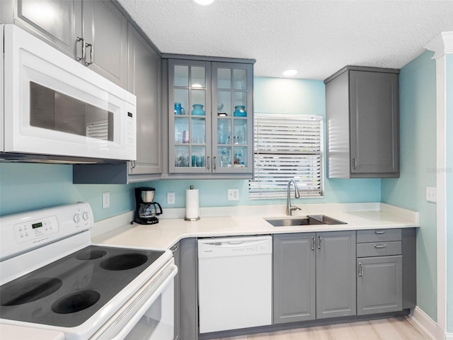 kitchen featuring gray cabinets, white appliances, glass insert cabinets, a textured ceiling, and a sink