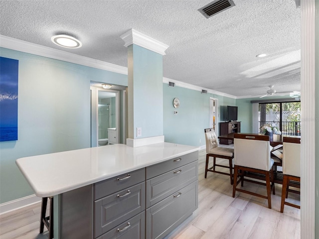 kitchen featuring visible vents, light countertops, a textured ceiling, gray cabinets, and light wood-style flooring