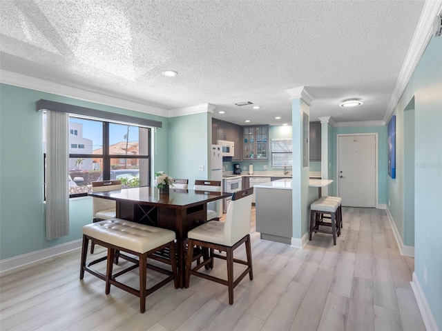 dining room featuring ornamental molding, baseboards, light wood-style floors, and a textured ceiling