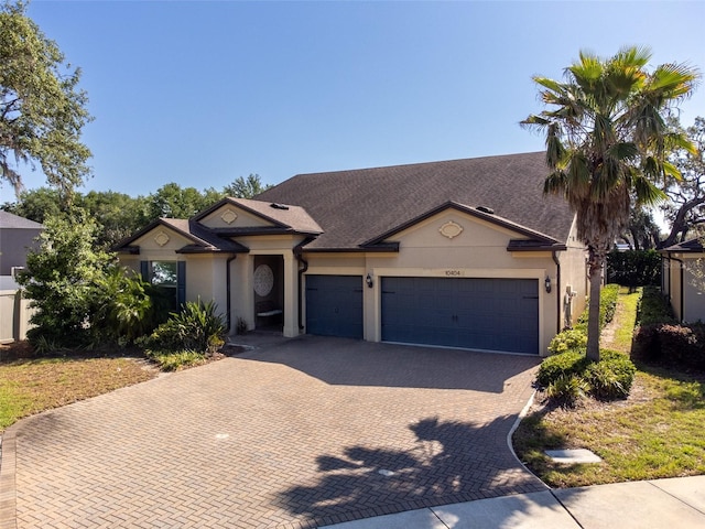 single story home featuring roof with shingles, stucco siding, decorative driveway, and an attached garage