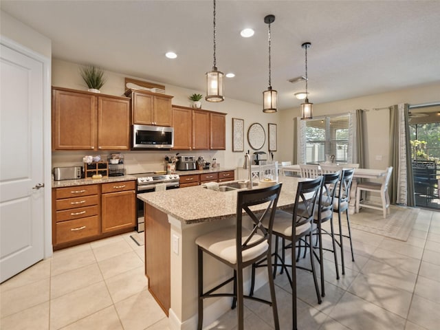kitchen with stainless steel appliances, brown cabinets, a sink, and a kitchen bar