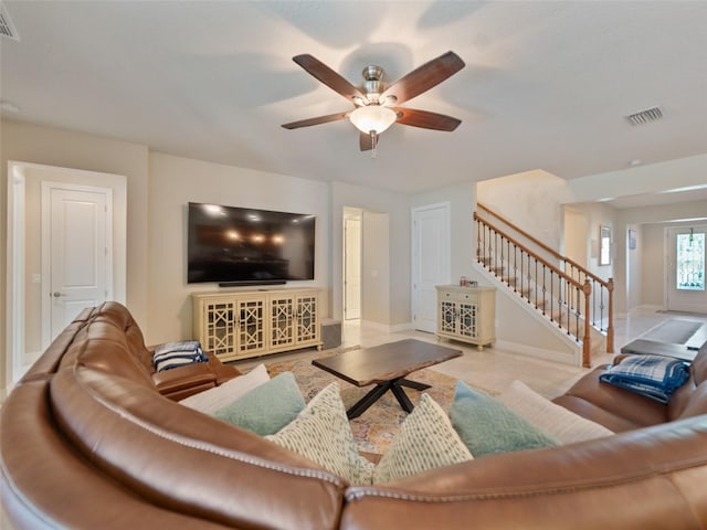 living room with stairway, visible vents, baseboards, and ceiling fan