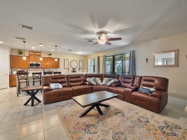living area with light tile patterned floors, visible vents, a textured ceiling, and ceiling fan