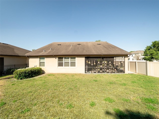 back of house featuring a yard, a fenced backyard, a sunroom, and stucco siding