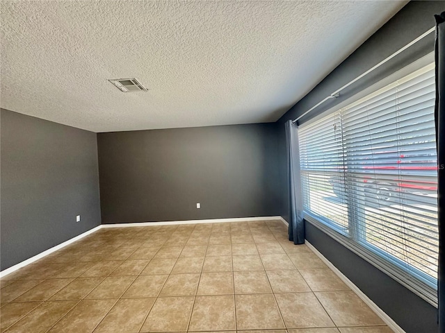 empty room featuring light tile patterned floors, a textured ceiling, and baseboards