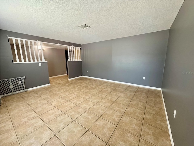 empty room with a textured ceiling, light tile patterned floors, and baseboards