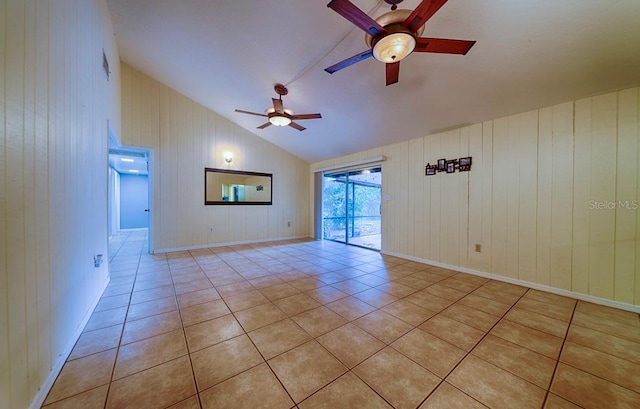 unfurnished room with vaulted ceiling, a ceiling fan, light tile patterned floors, and wood walls