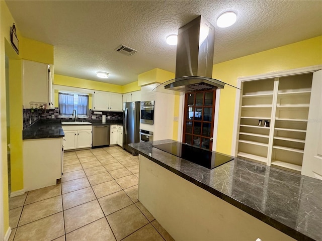 kitchen with island exhaust hood, stainless steel appliances, backsplash, a sink, and a textured ceiling