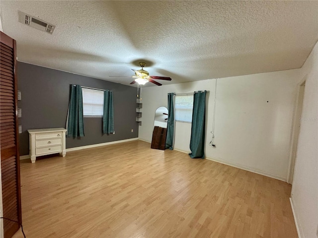 unfurnished bedroom with multiple windows, light wood finished floors, a textured ceiling, baseboards, and a ceiling fan