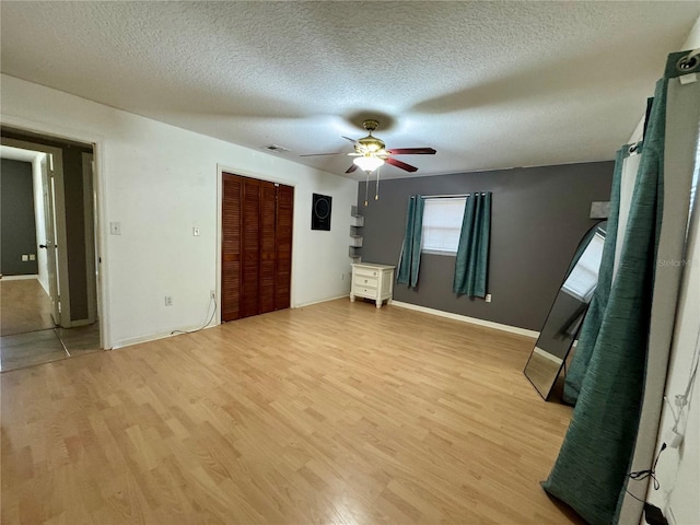 unfurnished bedroom with baseboards, light wood finished floors, a textured ceiling, ceiling fan, and a closet