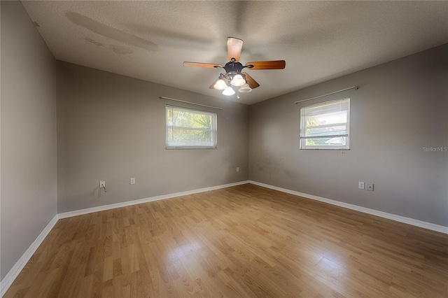 spare room featuring light wood finished floors, ceiling fan, baseboards, and a textured ceiling