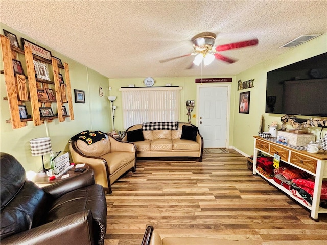 living area featuring visible vents, ceiling fan, light wood-style floors, and a textured ceiling