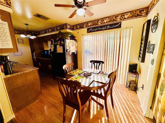 dining space with visible vents, light wood-type flooring, and a ceiling fan