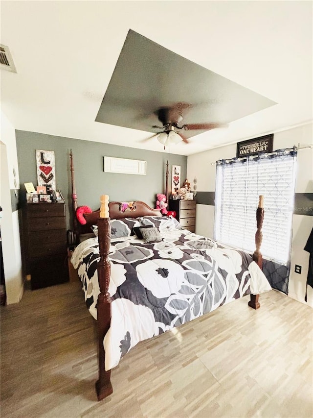 bedroom featuring ceiling fan, visible vents, a tray ceiling, and wood finished floors