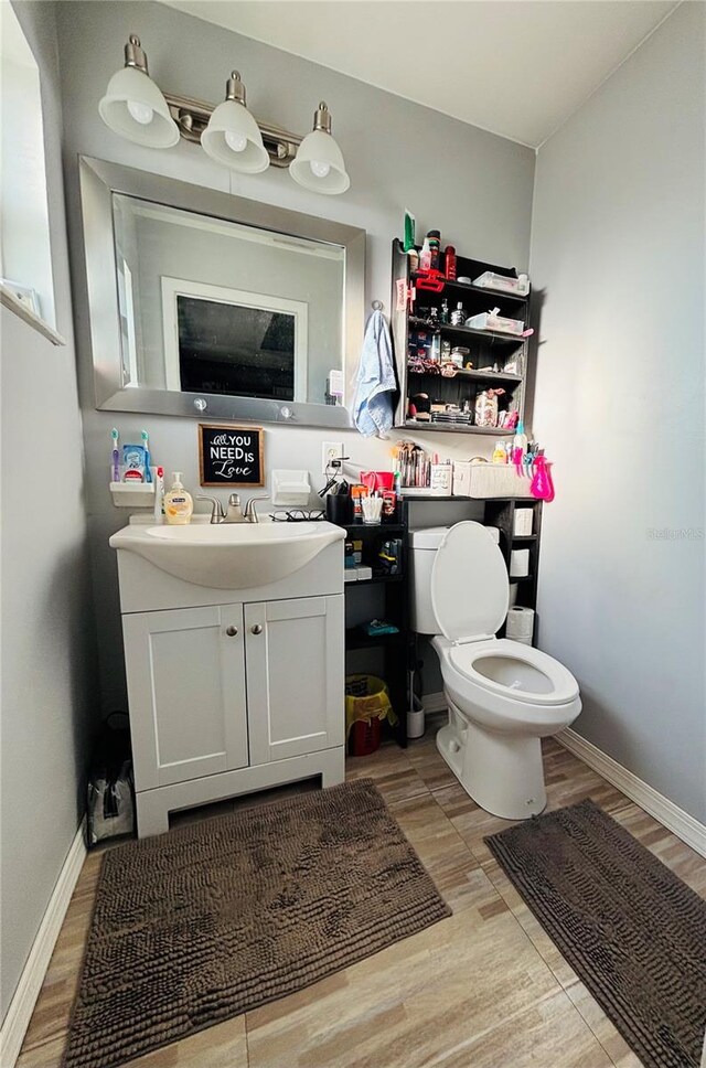 half bathroom featuring vanity, baseboards, toilet, and wood finished floors
