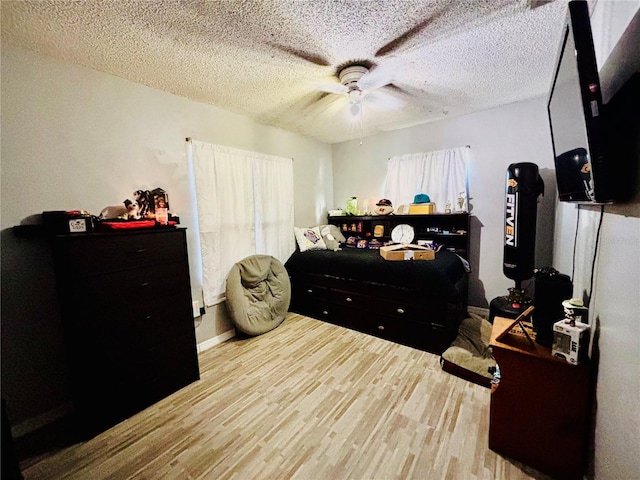bedroom with a ceiling fan, a textured ceiling, wood finished floors, and multiple windows