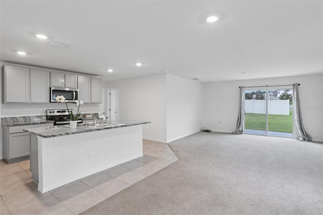 7530 Broad Pointe Dr, Zephyrhills, FL 33540 - kitchen featuring appliances with stainless steel finishes, gray cabinetry, recessed lighting, a center island with sink, and dark stone countertops